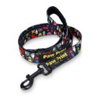 A colorful dog leash with various cartoon graphics featuring a black clasp. The leash has repeated Paw Print text in yellow. The graphics include playful images of animals and objects.