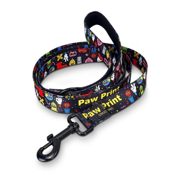 Black dog leash with colorful graphics includes bones, paws, and other playful symbols. The leash features a sturdy metal clip and Paw Print and Grow Wing in yellow text.