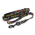 A colorful dog leash featuring cartoon-style prints, including various animals and playful designs. The leash shows the text Paw Print Grooming in yellow. It has a metal clasp for attaching to a collar.