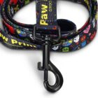 A colorful pet leash with various cartoon designs is coiled neatly. The leash features a black metal clasp and has the words Paw Prime Grooming printed on it along with vibrant images of animals, hearts, and pawprints.