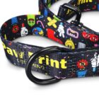 A colorful dog collar with cartoon characters and graphics. It features a black metal ring and the partially visible text Pawprint on a dark background. The design includes various playful images like flowers, hands, and abstract shapes.