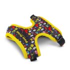 A colorful dog harness with yellow edging features various playful emojis and graphics against a black background. It includes adjustable straps and buckles for fastening.