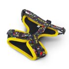 A colorful dog harness with a pattern of various small shapes and characters on a black background, outlined with bright yellow trim. It has adjustable straps and secure buckles, with a soft, breathable black inner lining.