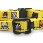 A yellow pet collar with black plastic buckle and adjustable slider. The fabric features a pattern of cartoon cat faces in black, gray, and orange.