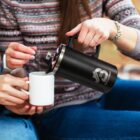 Person pouring coffee from a black French press into a white mug.