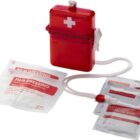 A compact red first aid kit with a white cross symbol, containing film dressings, waterproof plasters, and antiseptic cleansing wipes. It has a white lanyard attached.