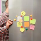 Child near an open fridge door with colorful sticky notes and magnets on it.