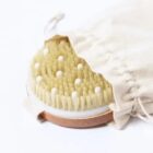 Dry brush with soft bristles and white massage nodules partially covered by a beige cloth bag.