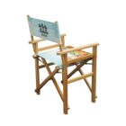 Wooden directors chair with a light blue fabric backrest featuring a Summer Breeze design with palm trees. The seat has a colorful abstract pattern. The chair is angled to the left.