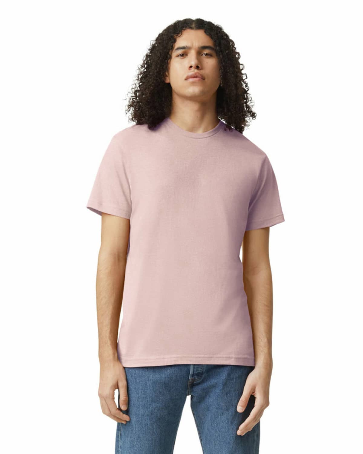 Person with long curly hair wearing a light pink t-shirt and blue jeans, standing facing forward.