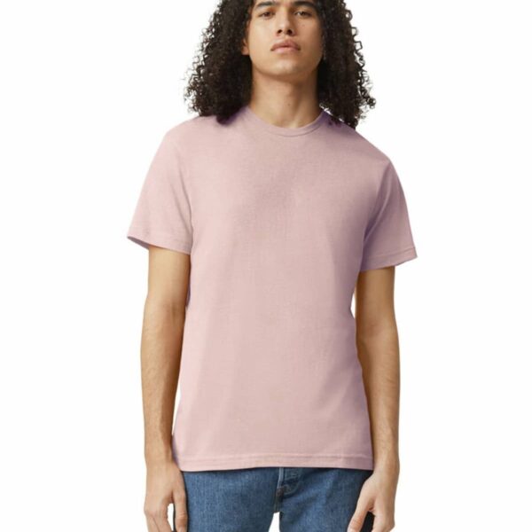 Person with curly hair wearing a light pink t-shirt and jeans, standing against a white background.