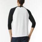 Person with cornrows wearing a black and white raglan shirt and jeans, seen from behind.