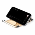 Smartphone on wooden stand with notebook and pens underneath.