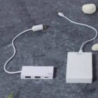 White USB hub and plug on a gray surface with small white stones.