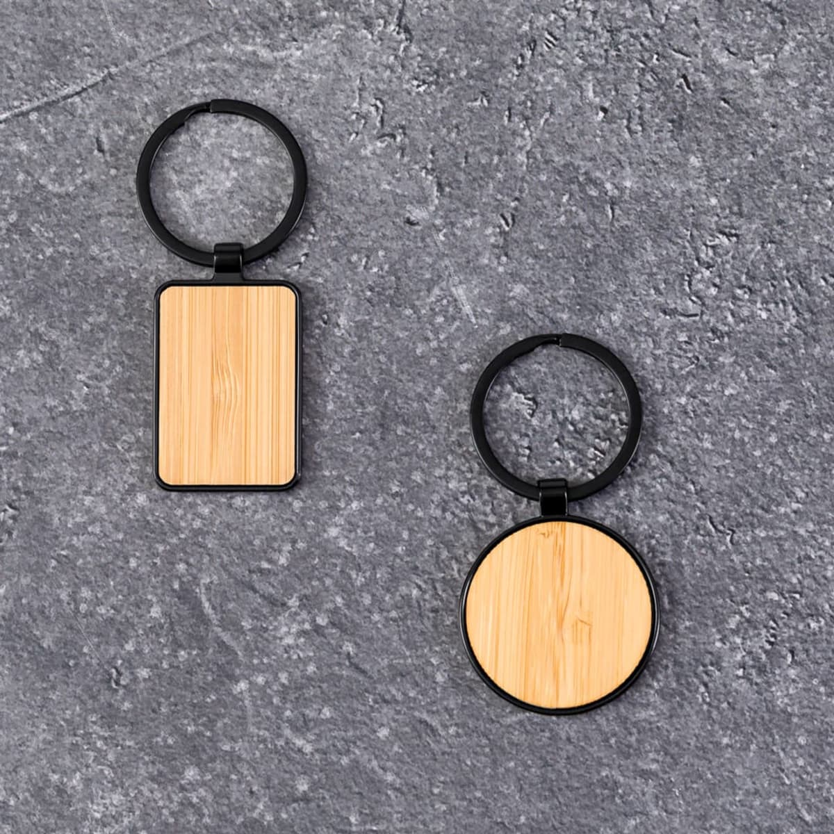Two wooden keychains, one rectangular and one circular, on a textured gray surface.