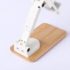 White mechanical arm on a wooden base against a plain background.