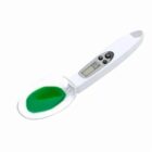 White digital measuring spoon with green liquid in scoop.