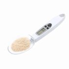 Digital measuring spoon with LCD display, holding a scoop of light brown powder.