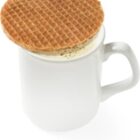 A stroopwafel resting on top of a white mug filled with coffee.