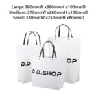 Three white shopping bags of different sizes with D.D. SHOP printed on them.