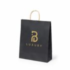 A black shopping bag with gold handles featuring a gold stylized B logo and the word LUXURY printed below it.