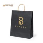 Black paper shopping bag with a gold logo featuring a stylized B and the word LUXURY below it. The handle is made of twisted paper. A small RECYCLED PAPER symbol appears in the top left corner.