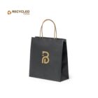 A black paper shopping bag with a brown handle and a gold geometric logo on the front. The text Recycled Paper with a recycling symbol is in the top left corner. The background is white.