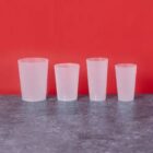 Four frosted plastic cups of varying sizes on a gray surface against a red background.