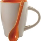 White mug with orange interior and matching orange spoon resting on the handle.