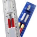 White and blue rulers holding red pencils and sharpeners, shown close up on a white background.