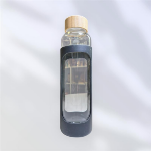 A sleek promotional glass water bottle with a wooden cap is enclosed in a black silicone sleeve, featuring an oval cutout. The soft, blurry background adds an elegant touch to its sophisticated design.