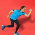 Person in blue and black running attire poses as if sprinting against a red background.