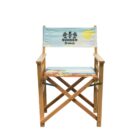 A wooden directors chair with a light blue fabric backrest featuring the words Summer Breeze and illustrations of palm trees and a sun. The seat has a colorful pattern with tropical designs.
