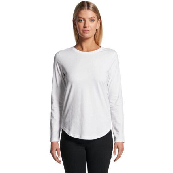 Woman in long-sleeve white shirt and black pants stands against a white background.