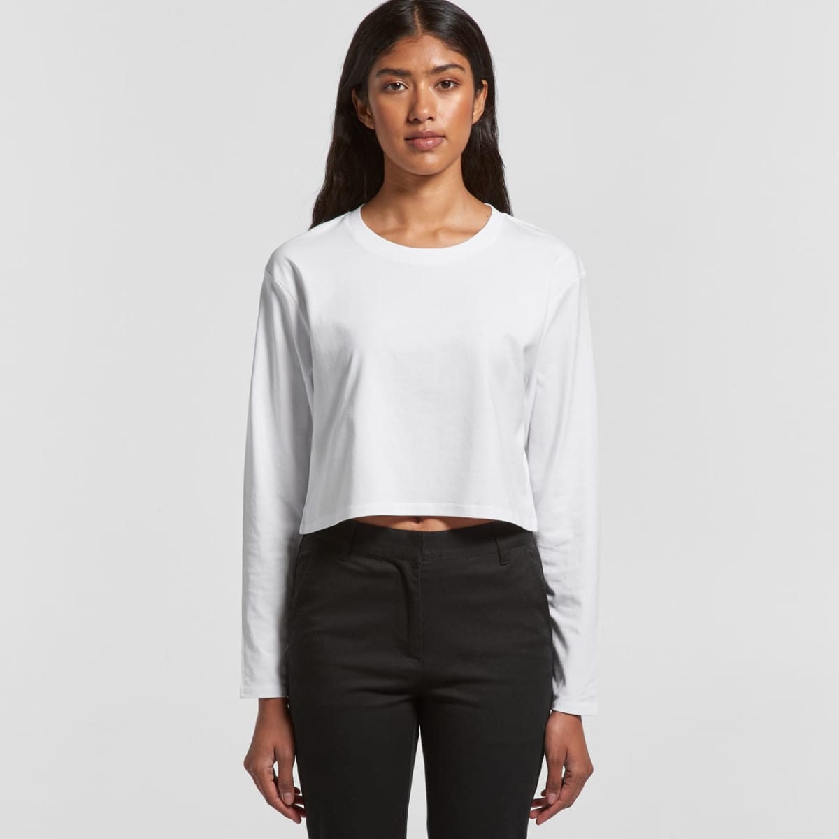 Person wearing a white long-sleeve crop top and black pants, standing against a plain background.