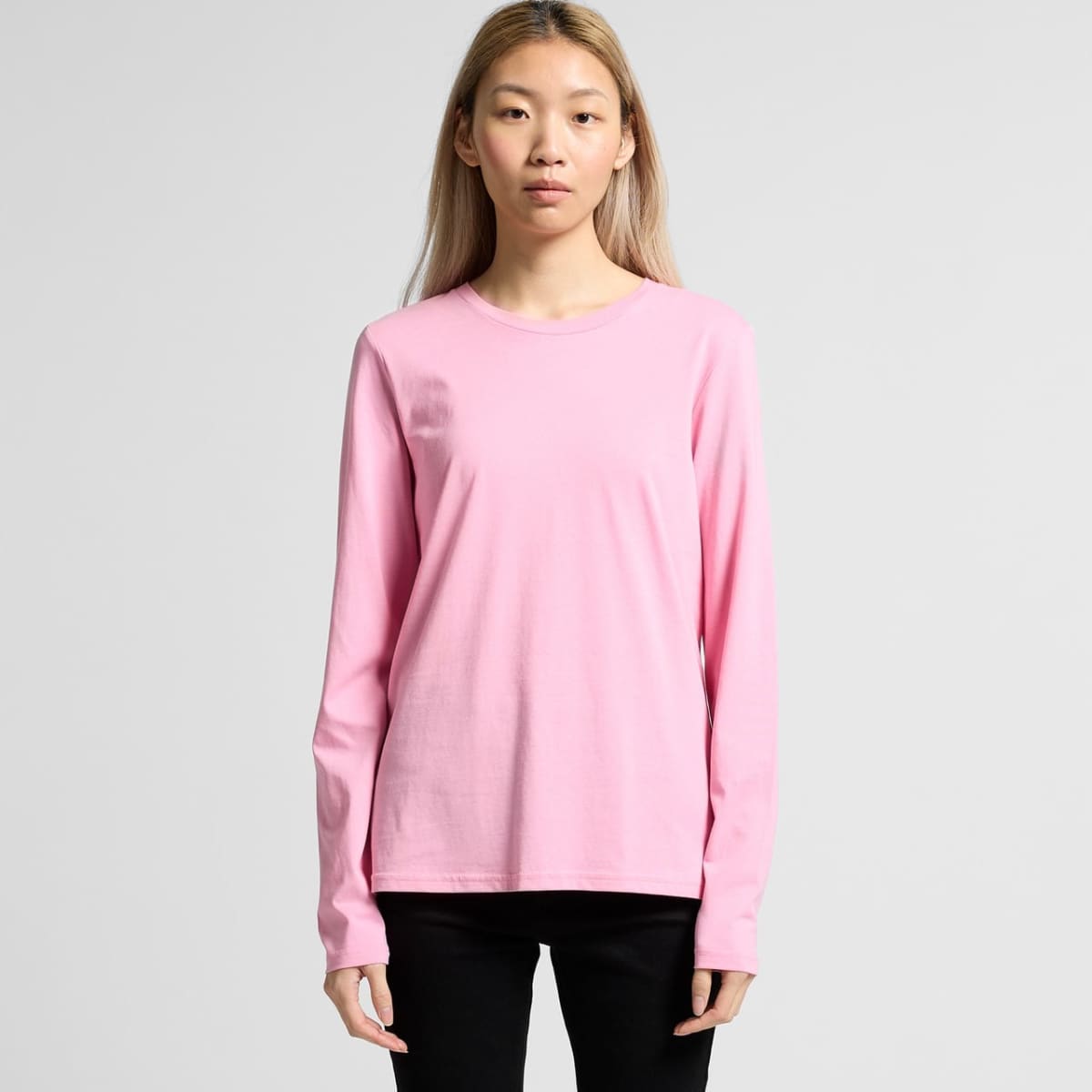 Person wearing a plain pink long-sleeve shirt and black pants, standing against a gray background.