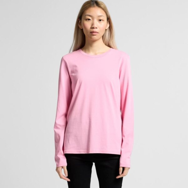 Person wearing a long-sleeved pink shirt and black pants standing against a plain background.