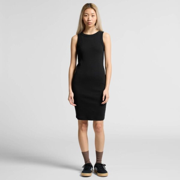 Woman in a sleeveless black dress with sneakers standing against a plain light background.