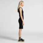 Woman in a black sleeveless dress and sneakers standing in profile against a plain background.