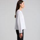 Woman in a white long-sleeve shirt and black pants standing in profile against a gray background.