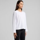Woman in a plain white long-sleeve shirt and black pants standing against a gray background.
