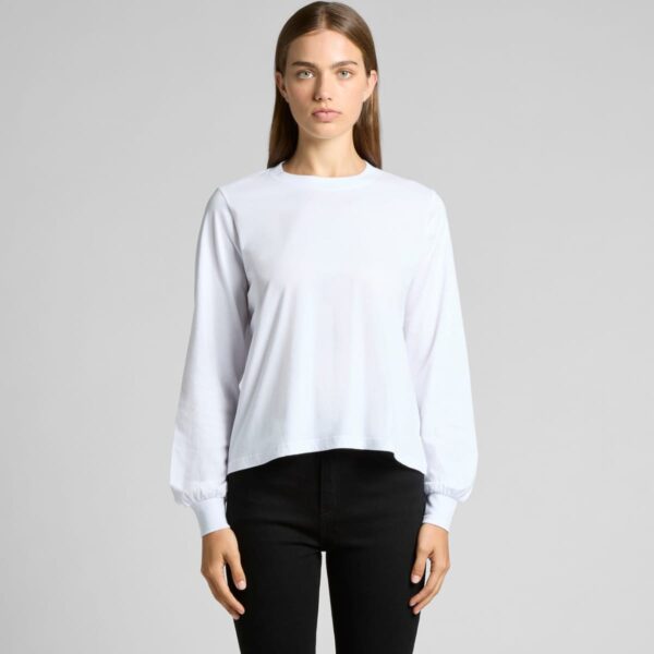Person in a white long-sleeve shirt and black pants against a gray background.
