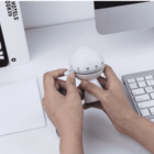 Hands adjusting a white kitchen timer near a keyboard on a desk.