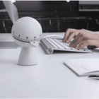 Person typing on a keyboard with a timer and notebook on the desk.