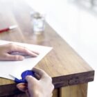 Person using correction tape on paper at a wooden table.