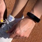 Person tying white sneaker laces, wearing a black fitness tracker on wrist.