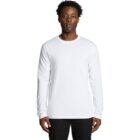 Man in a white long-sleeve shirt and black pants standing against a plain white background.