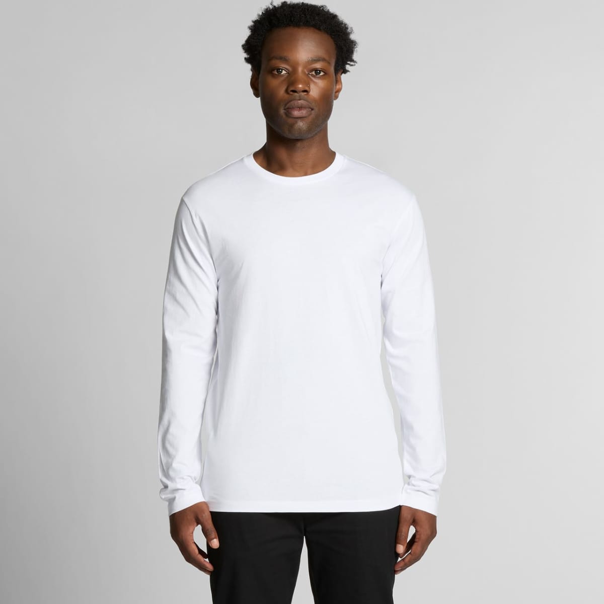 Person in a white long-sleeve shirt and black pants standing against a gray background.