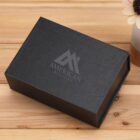 Black gift box with American Real Estate logo on a wooden surface.