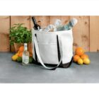 White tote bag with groceries, wine, and drinks; surrounded by citrus fruits and a basil plant.